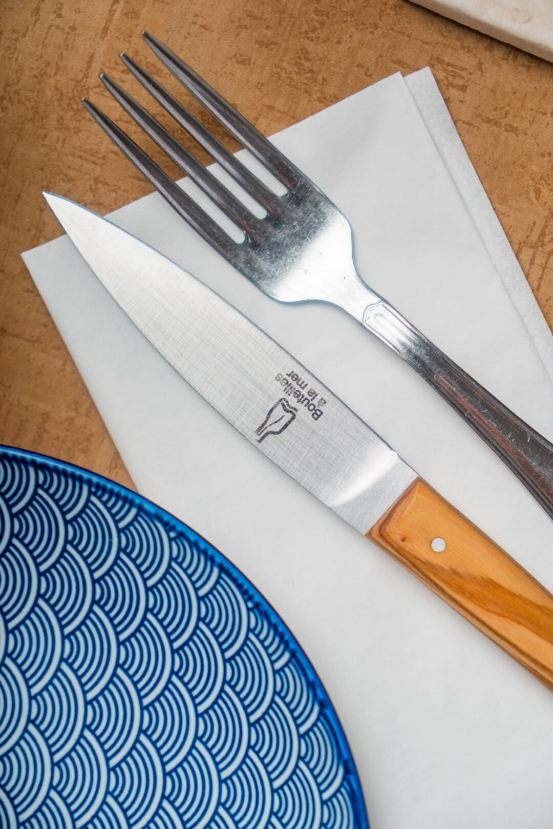 Couteau gravé avec le logo Bouteilles à la mer et fourchette posés sur une serviette à côté d'une assiette.