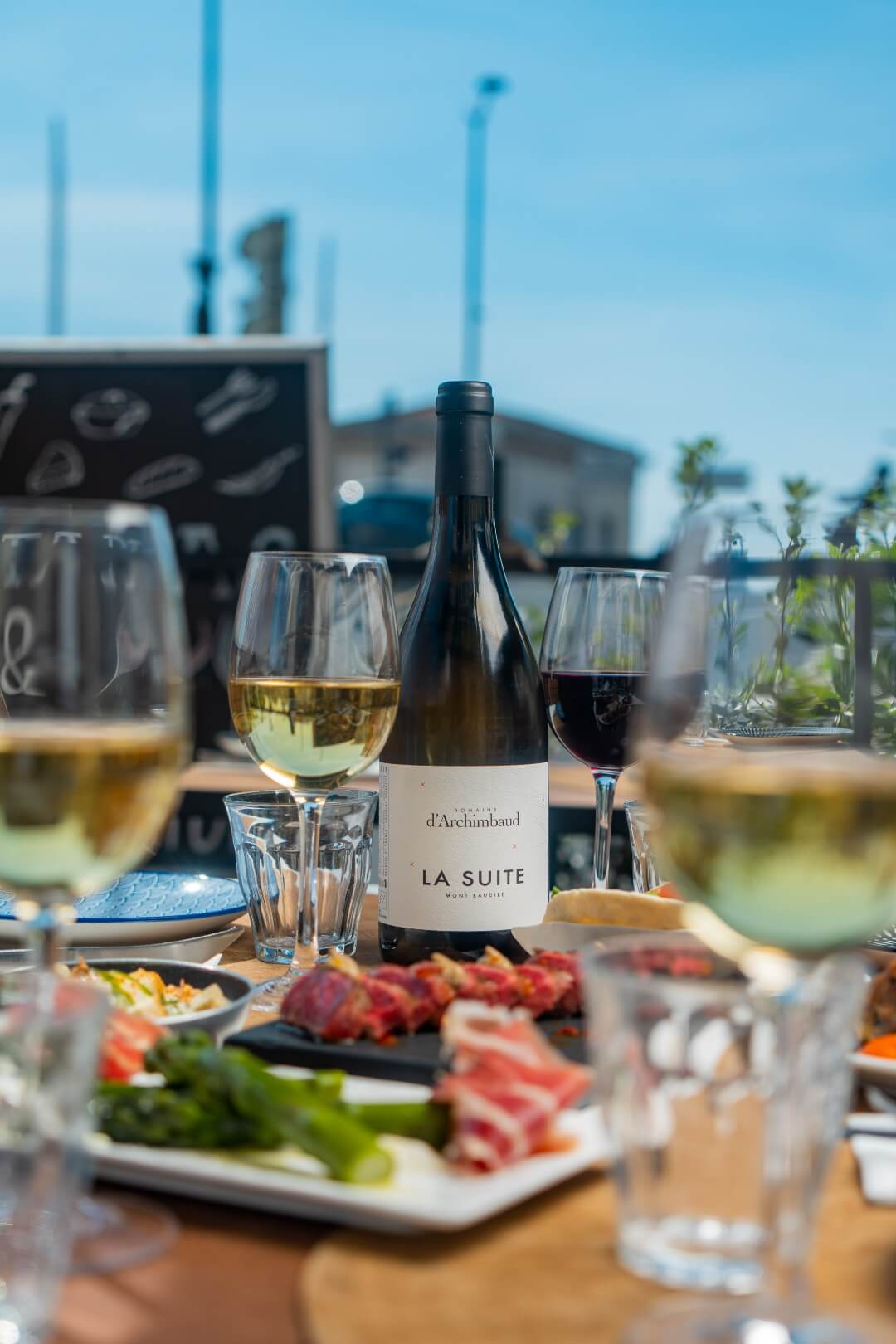 Différents tapas disposés sur une table en terrasse avec une bouteille de vin du domaine archimbaud.