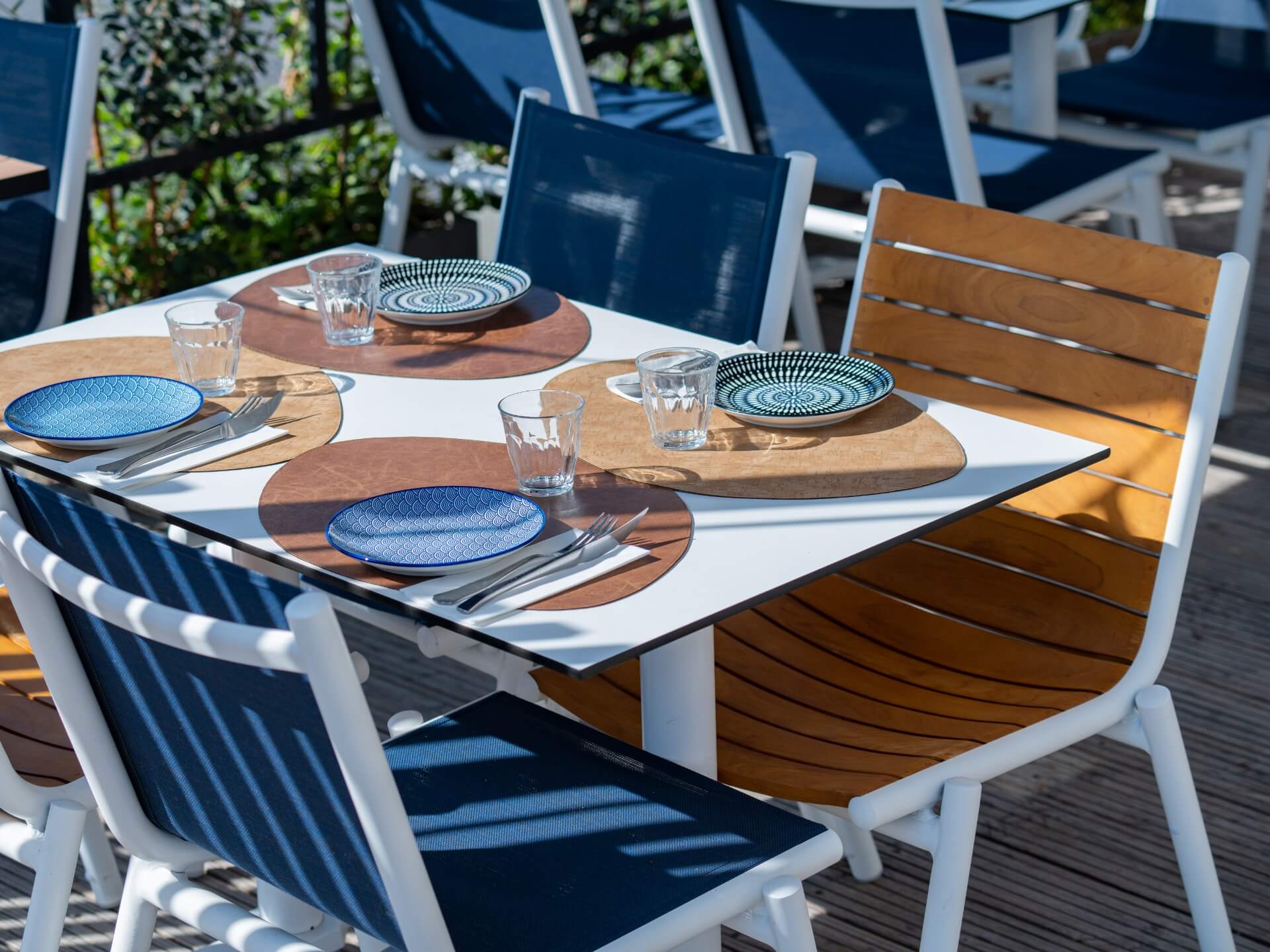 Grande table et quatre chaises design en bois et métal, avec le couvert mis et le soleil du sud..